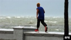 Un joven camina por el muro del malecón de Cienfuegos.