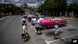 Turistas pasan frente a un estacionamiento de autos clásicos estadounidenses que esperan clientes, en La Habana, Cuba, el 9 de julio de 2022. (Foto AP/Ramón Espinosa)