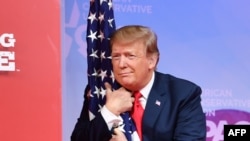 El presidente Donald Trump abraza la bandera de los EEUU, momentos antes de hablar en la Conferencia anual de Acción Política Conservadora (CPAC) en National Harbor, Maryland, el 2 de marzo de 2019.