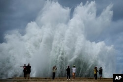 La gente toma fotografías de las olas que se estrellan contra el muro del Malecón, provocado por el paso del huracán Milton en el Golfo de México, en La Habana, Cuba, el miércoles 9 de octubre de 2024. (Foto AP/Ramon Espinosa)