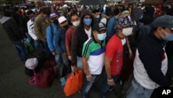 Viajeros en una terminal de Bogotá, Colombia, esperan en línea para abordar un ómnibus. 