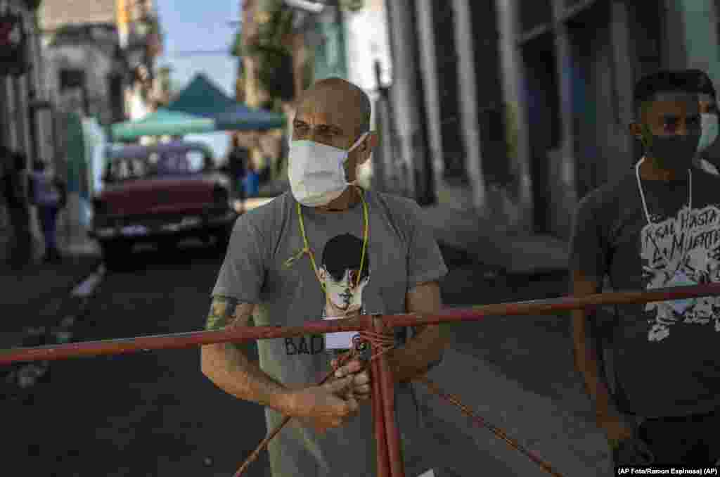 Hombres montan guardia en una reja que corta el acceso a su vecindario para mantener alejados a los que no viven allí, como una forma de frenar la propagación de COVID-19 en La Habana, Cuba, el lunes 22 de febrero de 2021. (AP Foto/Ramon Espinosa)