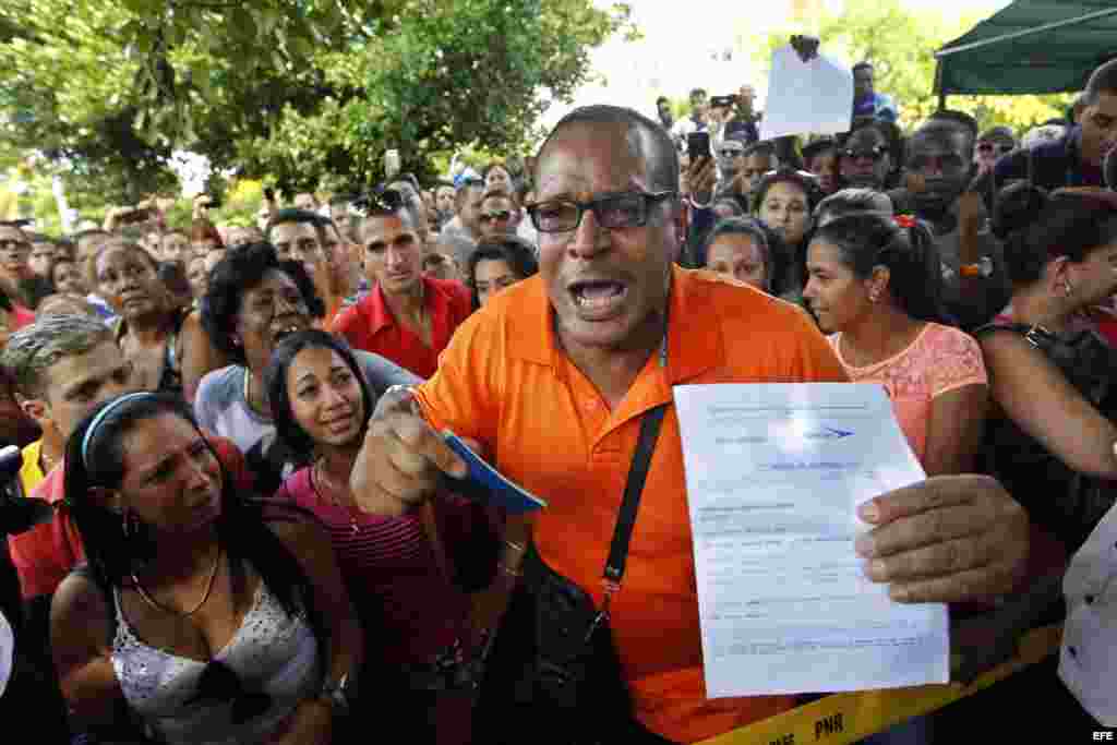 Un hombre, con un pasaporte en su mano y algunos documentos que confirman sus planes de viaje, protesta frente a la embajada de Ecuador en La Habana.