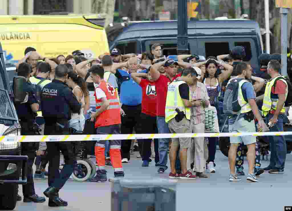 Un grupo de gente con los brazos en alto ante el despliegue policial en el lugar del atentado ocurrido hoy en las Ramblas de Barcelona.