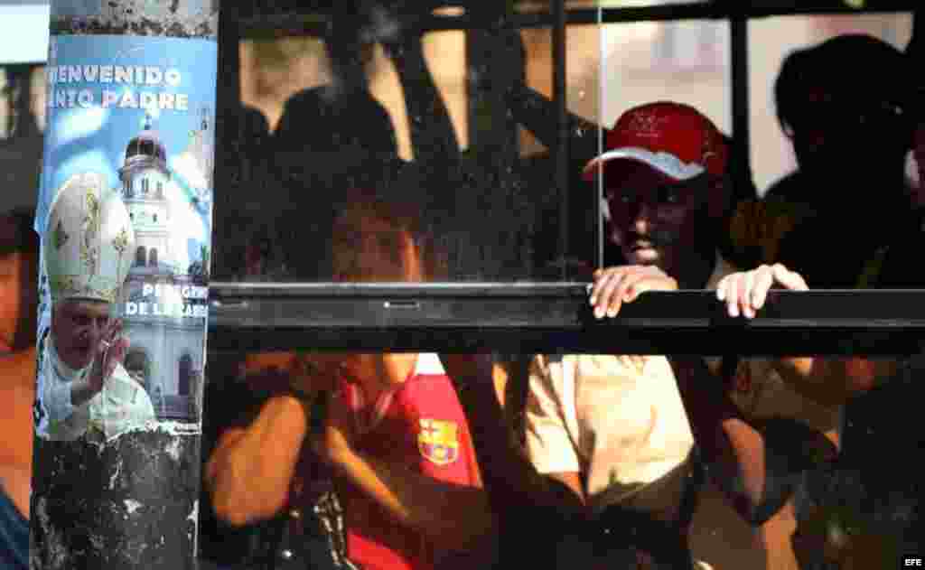 Pasajeros de un bus cruzan frente a un cartel de bienvenida al papa Benedicto XVI hoy, lunes 19 de marzo, en La Habana (Cuba). El Pontífice llegará a la isla el próximo día 26 para una visita de tres días.