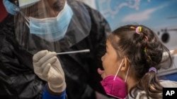 Una empleada de salud toma una muestra para una prueba de COVID-19 a una niña procedente de México, en el Aeropuerto Internacional José Martí de La Habana.